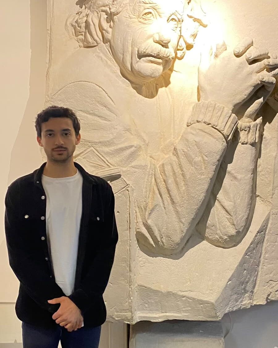 Hussien Ballouk standing in front of a sculpted Albert Einstein relief